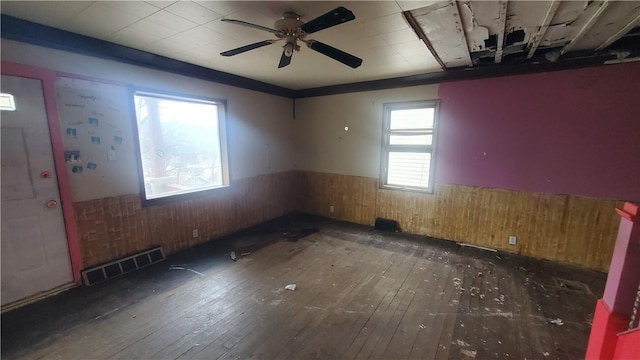 spare room with wood-type flooring, wainscoting, ceiling fan, and wood walls