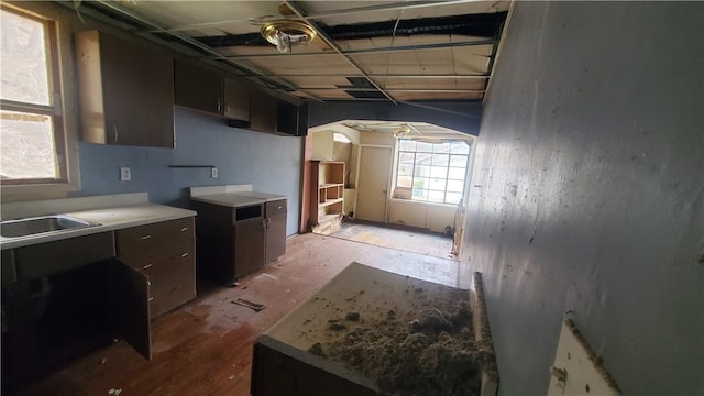kitchen with arched walkways, a sink, light countertops, dark brown cabinets, and light wood-style floors