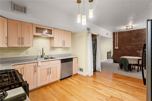 kitchen with stainless steel appliances, a sink, stacked washing machine and dryer, light brown cabinets, and light wood-style flooring