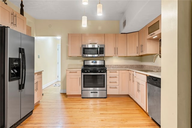 kitchen with appliances with stainless steel finishes, a sink, light brown cabinetry, light countertops, and light wood finished floors