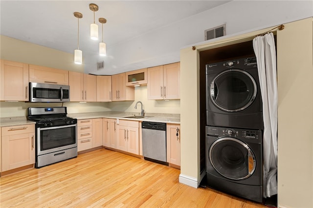 kitchen featuring appliances with stainless steel finishes, stacked washer and clothes dryer, a sink, and light countertops