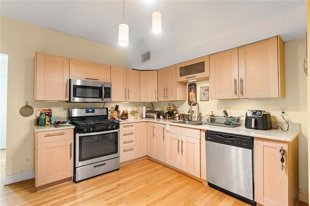 kitchen featuring stainless steel appliances, light brown cabinetry, a sink, and light wood-type flooring