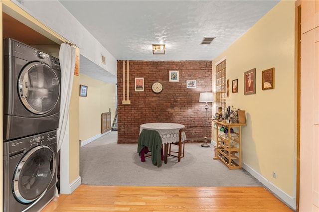 clothes washing area featuring stacked washer / dryer, brick wall, wood finished floors, a textured ceiling, and baseboards
