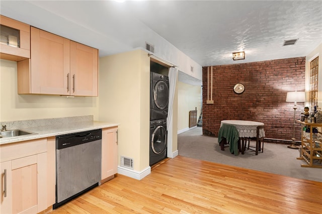 kitchen with stainless steel dishwasher, stacked washer and clothes dryer, brick wall, light wood-style floors, and baseboards