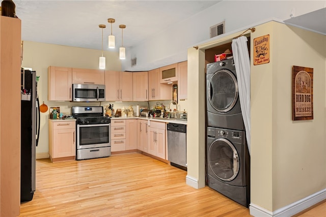 kitchen with stainless steel appliances, stacked washer and clothes dryer, light wood finished floors, light brown cabinetry, and light countertops