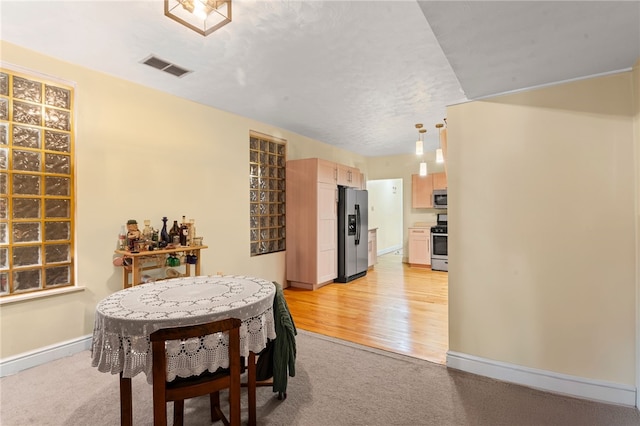 dining space with baseboards, light carpet, and light wood-style flooring