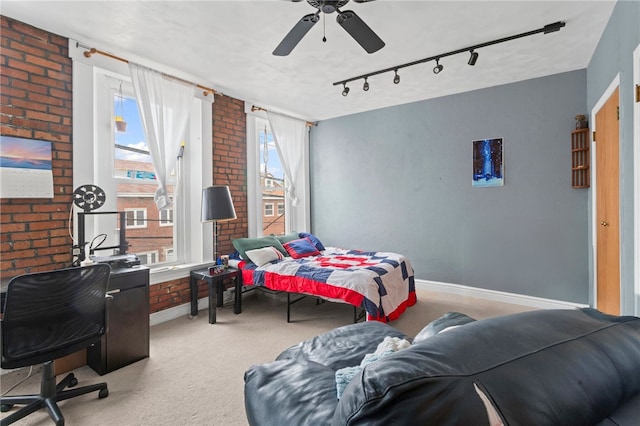 bedroom with light carpet, multiple windows, rail lighting, brick wall, and baseboards