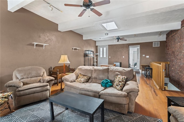 living room with ceiling fan, light wood-style flooring, beamed ceiling, a skylight, and rail lighting