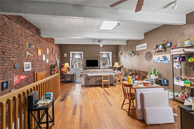 dining space with ceiling fan, light wood-style floors, beamed ceiling, a skylight, and brick wall