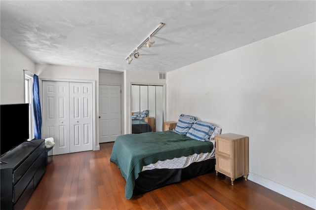 bedroom featuring track lighting, two closets, and hardwood / wood-style floors