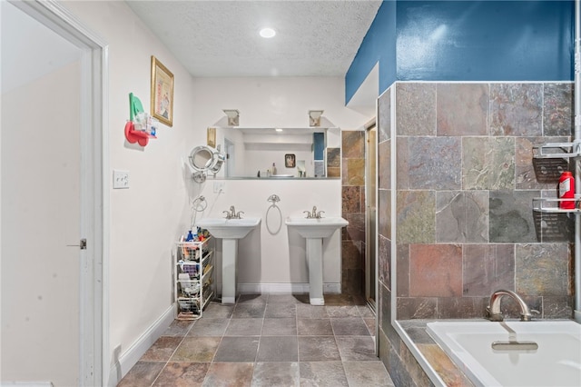 bathroom featuring a textured ceiling, tiled tub, a sink, recessed lighting, and baseboards