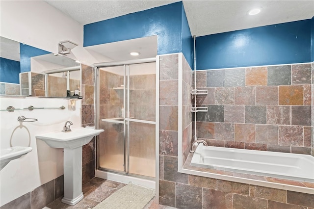bathroom with a stall shower, tiled tub, stone tile floors, a textured ceiling, and tile walls