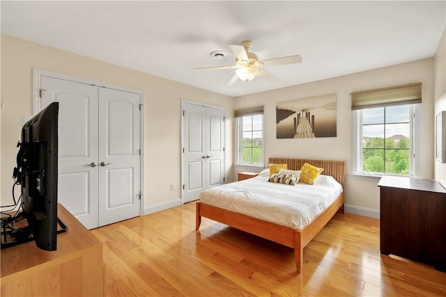 bedroom featuring two closets, light wood finished floors, baseboards, and a ceiling fan