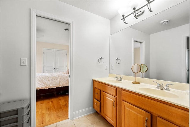 ensuite bathroom featuring tile patterned floors, double vanity, and baseboards