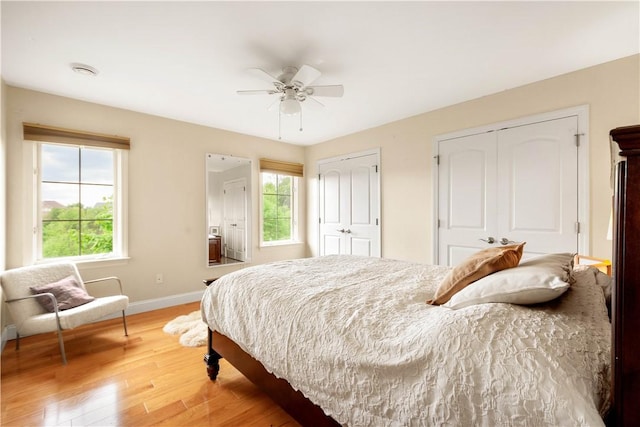 bedroom with multiple closets, baseboards, light wood finished floors, and multiple windows