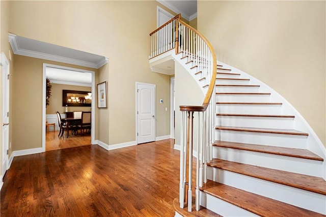 stairway with crown molding, wood finished floors, baseboards, and a towering ceiling