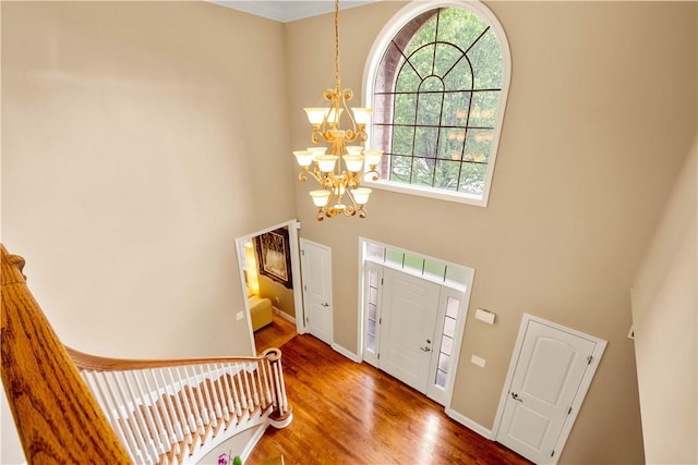 entryway with a towering ceiling, a chandelier, wood finished floors, and baseboards