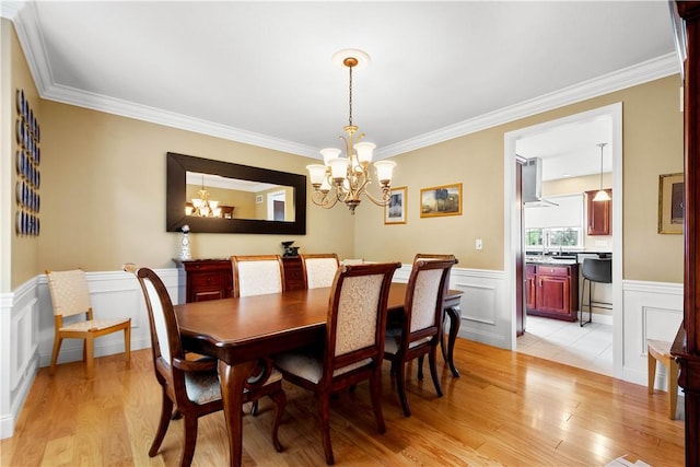 dining area featuring a chandelier, light wood-type flooring, crown molding, a wainscoted wall, and a decorative wall
