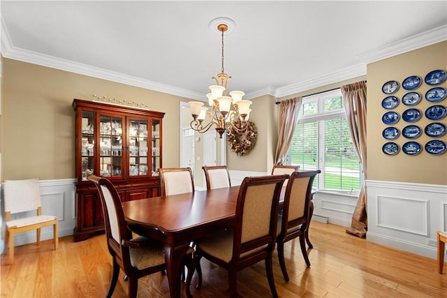 dining room featuring a chandelier, light wood-style flooring, wainscoting, ornamental molding, and a decorative wall