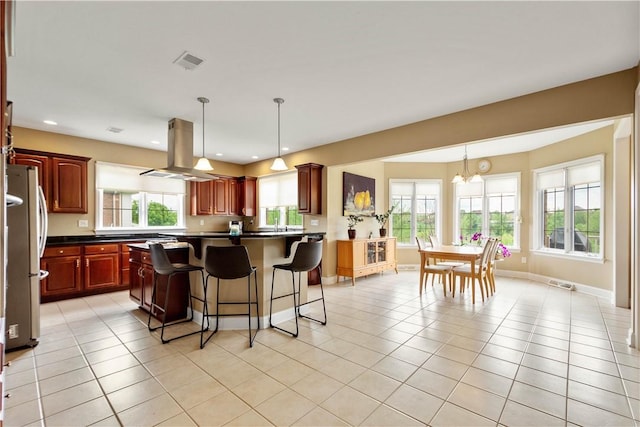 kitchen featuring island exhaust hood, freestanding refrigerator, a kitchen breakfast bar, dark countertops, and light tile patterned flooring