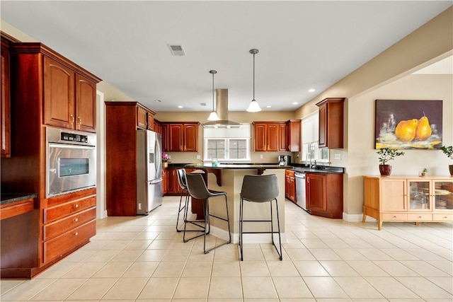 kitchen with stainless steel appliances, dark countertops, island exhaust hood, reddish brown cabinets, and a breakfast bar area