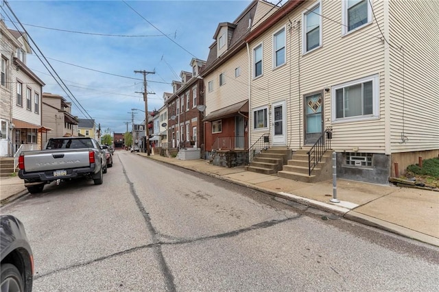 view of asphalt road with sidewalks, curbs, a residential view, and entry steps