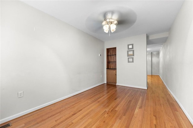 empty room with light wood finished floors, a ceiling fan, and baseboards