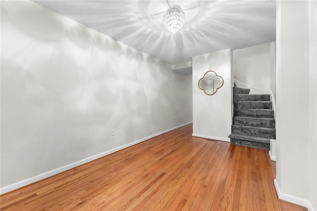 below grade area featuring wood finished floors, stairs, a chandelier, and baseboards