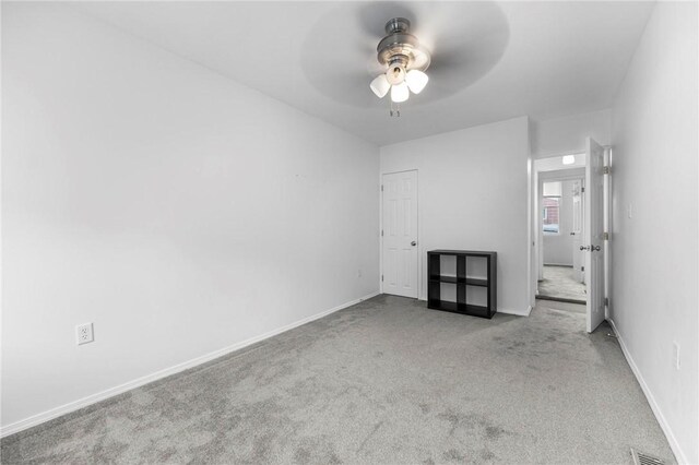 carpeted spare room featuring a ceiling fan and baseboards