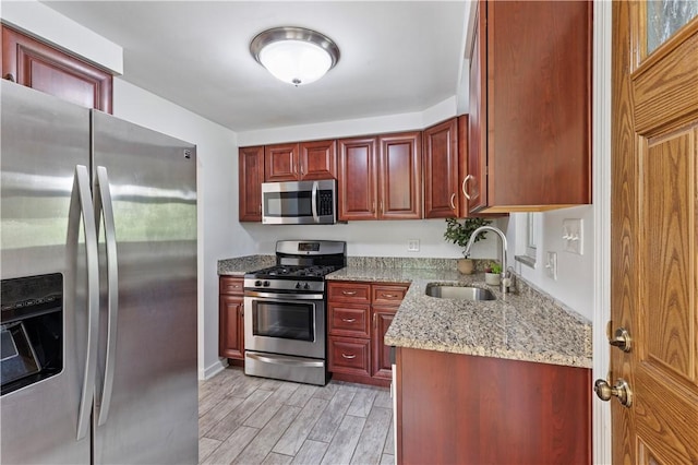 kitchen featuring appliances with stainless steel finishes, a sink, reddish brown cabinets, and light wood-style flooring