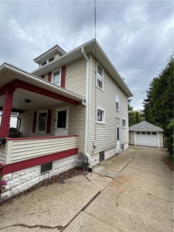 view of side of property with an outbuilding, a detached garage, driveway, and a porch