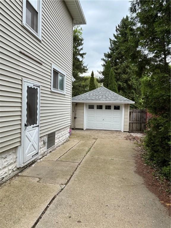view of home's exterior featuring an outbuilding, a detached garage, concrete driveway, and fence