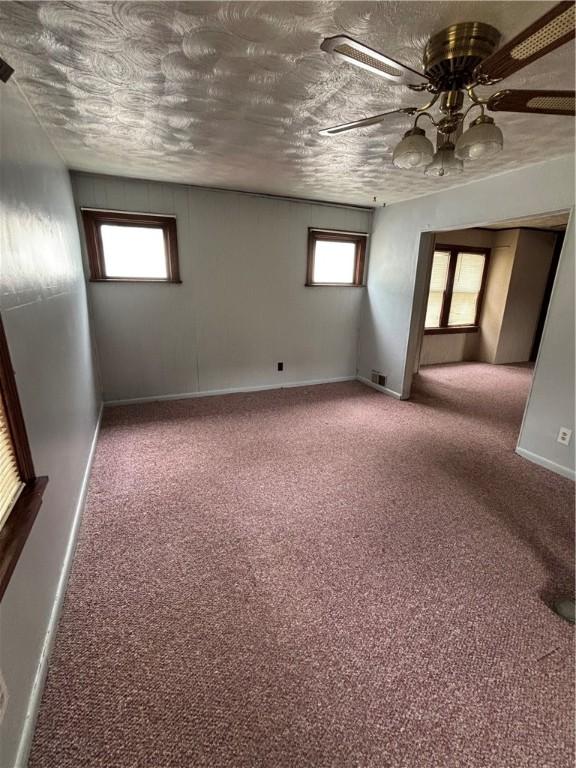 carpeted spare room featuring plenty of natural light, baseboards, and a ceiling fan