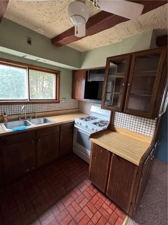 kitchen with gas range gas stove, a sink, backsplash, brick patterned floors, and beam ceiling