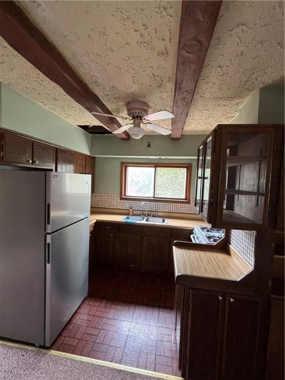 kitchen with freestanding refrigerator, a sink, beamed ceiling, ceiling fan, and light countertops