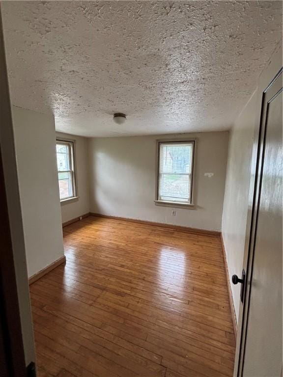 unfurnished room featuring light wood-type flooring, a textured ceiling, and baseboards