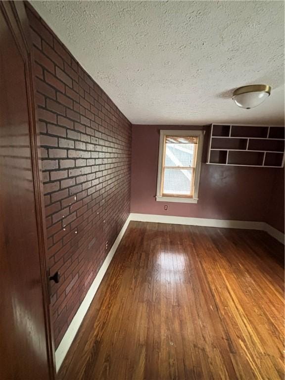 empty room featuring a textured ceiling, brick wall, dark wood finished floors, and baseboards
