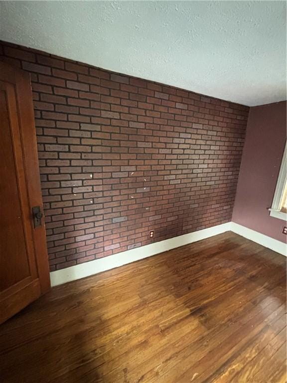 empty room featuring wood finished floors, a textured ceiling, baseboards, and brick wall