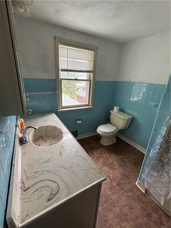 bathroom featuring tile patterned flooring, toilet, vanity, wainscoting, and tile walls