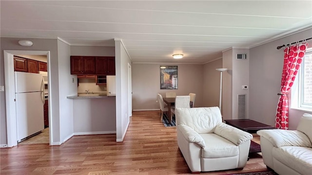 living area featuring light wood-style floors, baseboards, and crown molding