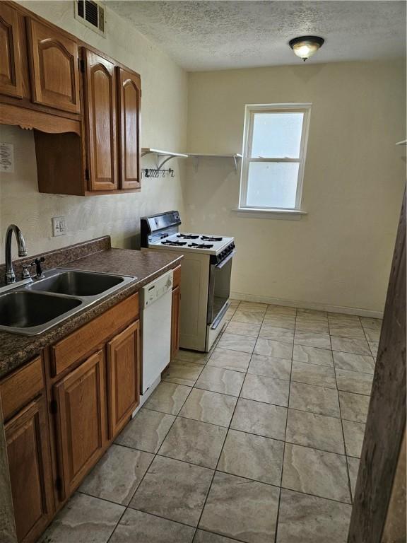kitchen featuring gas range oven, white dishwasher, a sink, dark countertops, and a textured ceiling
