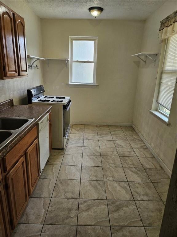 kitchen featuring range with gas cooktop, dishwasher, dark countertops, a textured ceiling, and a sink