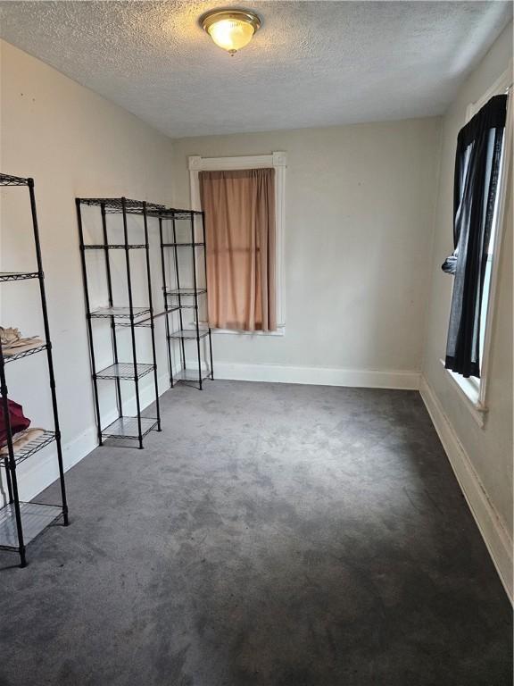 spare room with a textured ceiling, baseboards, and dark carpet