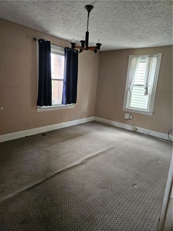 carpeted spare room featuring a chandelier, baseboards, and a textured ceiling