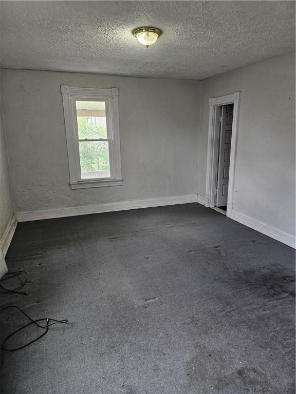 spare room with a textured ceiling, dark carpet, and baseboards