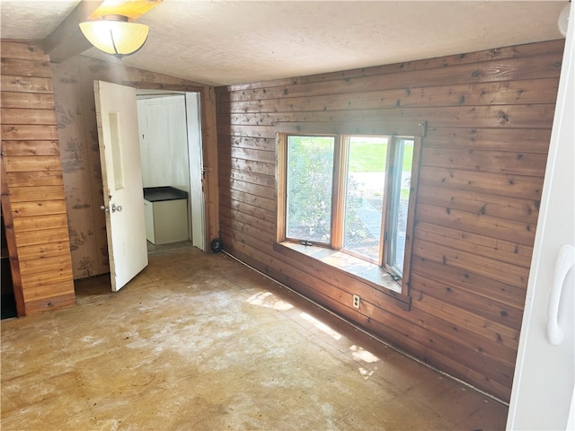 empty room featuring wooden walls, lofted ceiling, and a textured ceiling