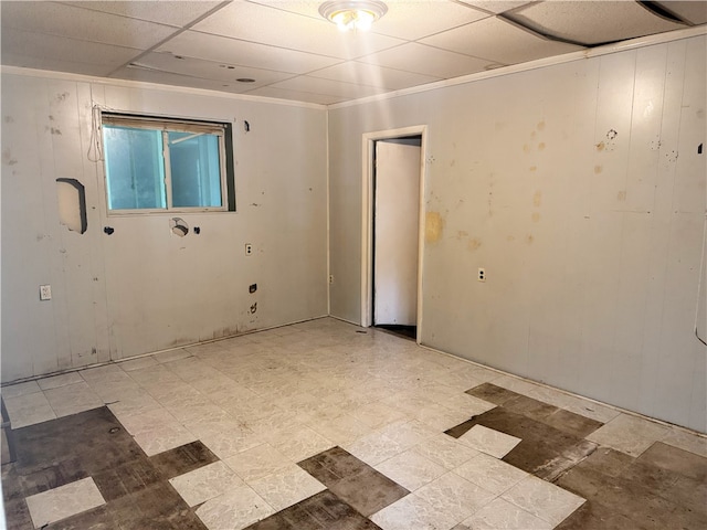 unfurnished room with light flooring, a drop ceiling, and wooden walls