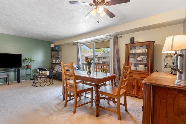 dining space featuring light carpet, ceiling fan, and a textured ceiling