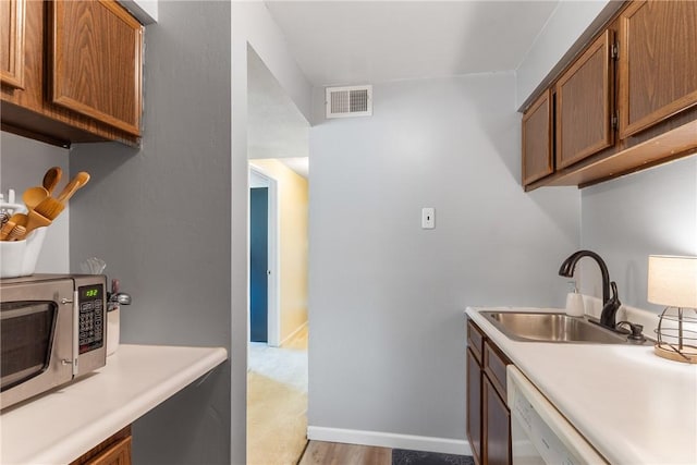 kitchen featuring a sink, stainless steel microwave, light countertops, and dishwasher