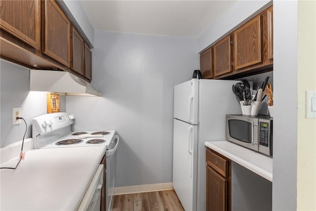 kitchen with white appliances, light wood-style flooring, under cabinet range hood, light countertops, and brown cabinetry